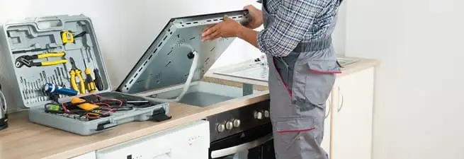 Cooktop repair technician lifting a built-in stovetop for service in Pembroke Pines, FL