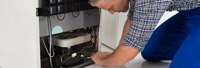 Refrigerator repair technician servicing the compressor and condenser area in Pembroke Pines, FL
