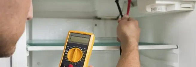 Refrigerator repair technician testing electrical components with a multimeter in Pembroke Pines, FL